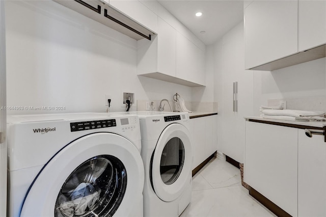 clothes washing area featuring light tile patterned flooring, washing machine and clothes dryer, and cabinets