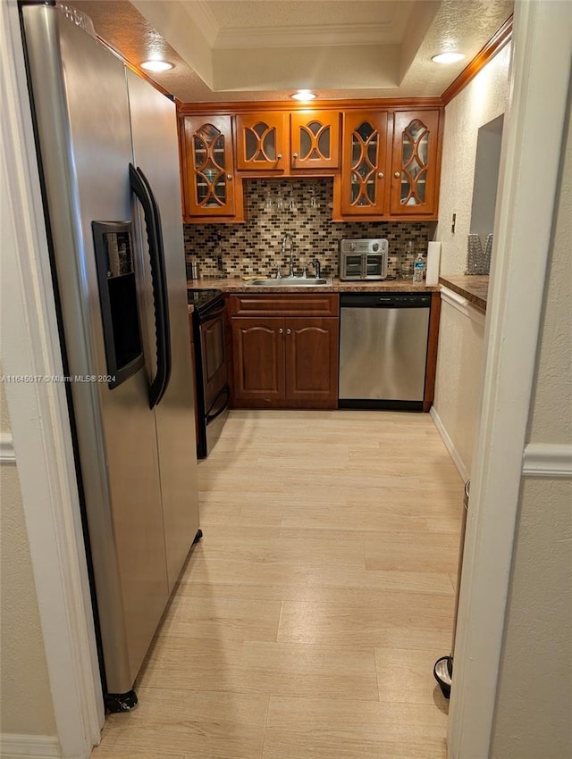 kitchen with a raised ceiling, glass insert cabinets, stainless steel appliances, crown molding, and a sink