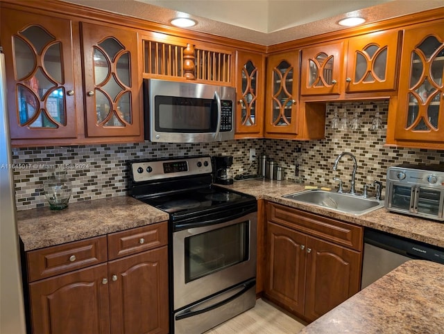 kitchen with tasteful backsplash, brown cabinetry, glass insert cabinets, appliances with stainless steel finishes, and a sink