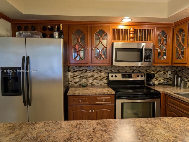 kitchen featuring brown cabinets, tasteful backsplash, glass insert cabinets, and stainless steel appliances