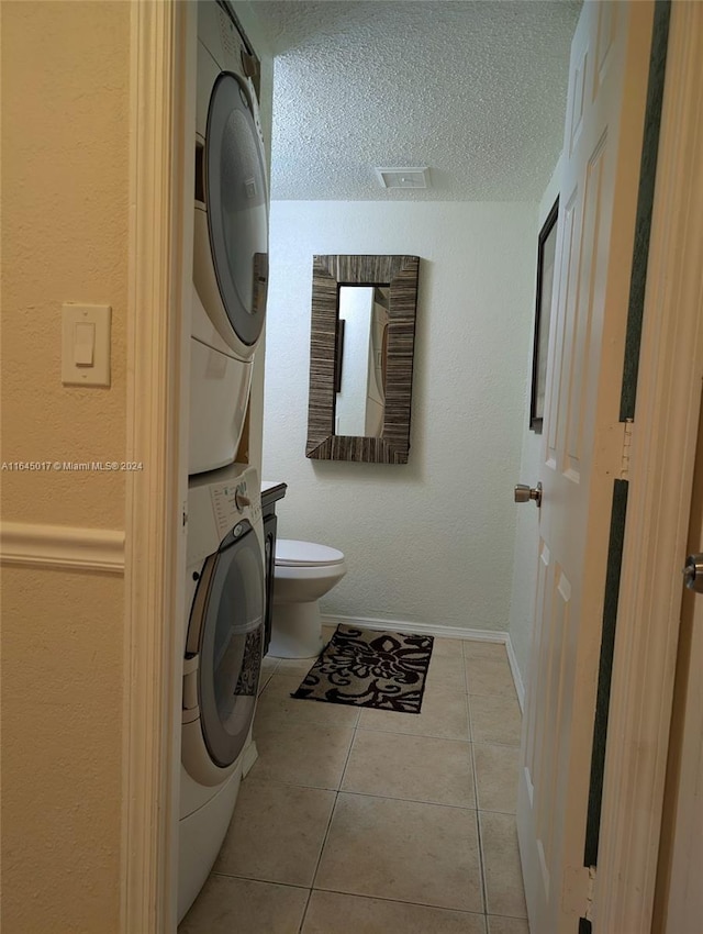 half bathroom featuring a textured ceiling, tile patterned flooring, toilet, stacked washer and dryer, and baseboards