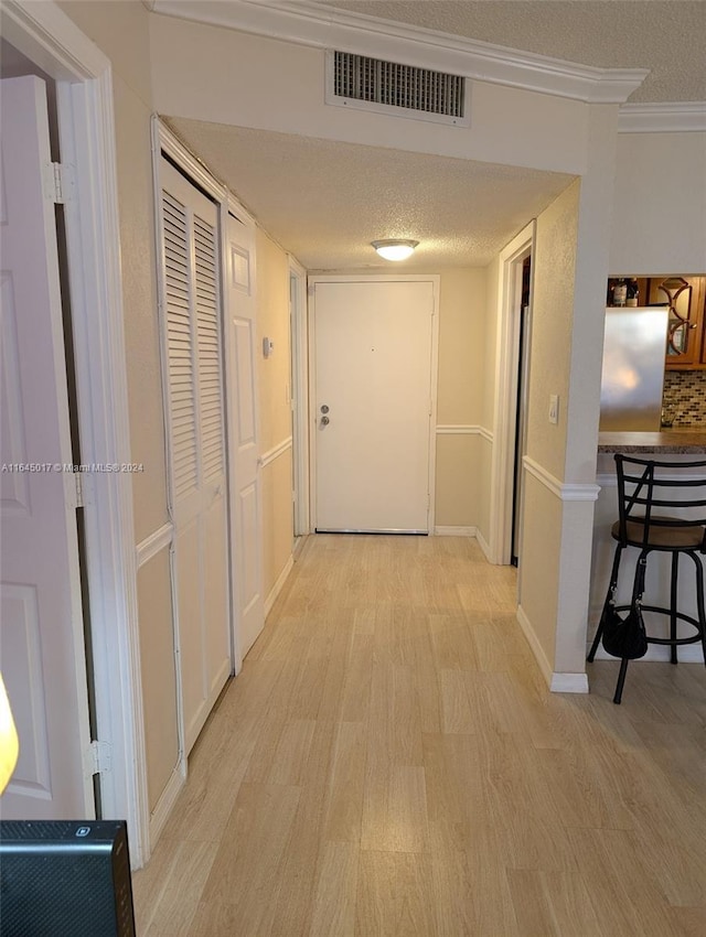 hall featuring light wood-style flooring, visible vents, and a textured ceiling