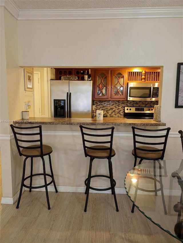 kitchen featuring stainless steel appliances, crown molding, backsplash, and a breakfast bar area