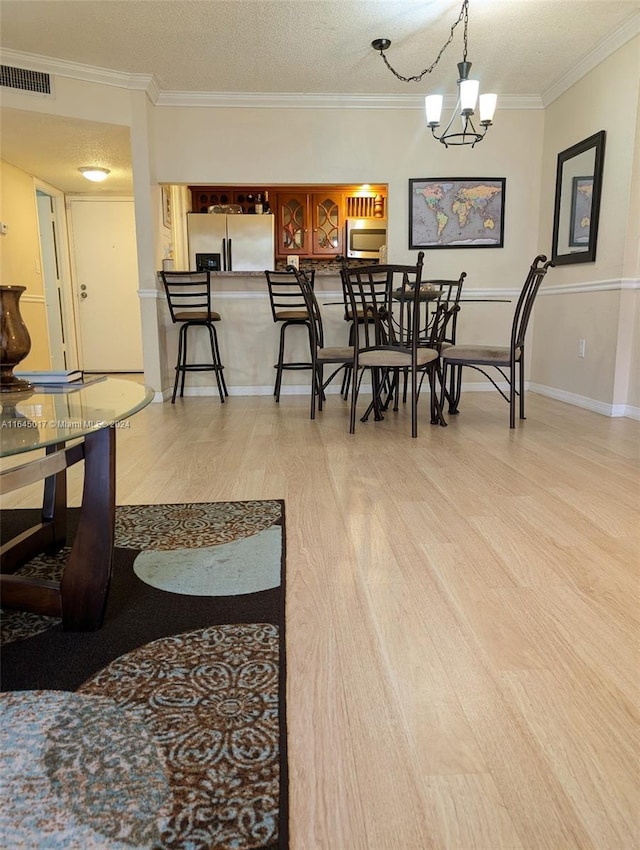 dining room featuring a textured ceiling, ornamental molding, light wood-type flooring, and visible vents