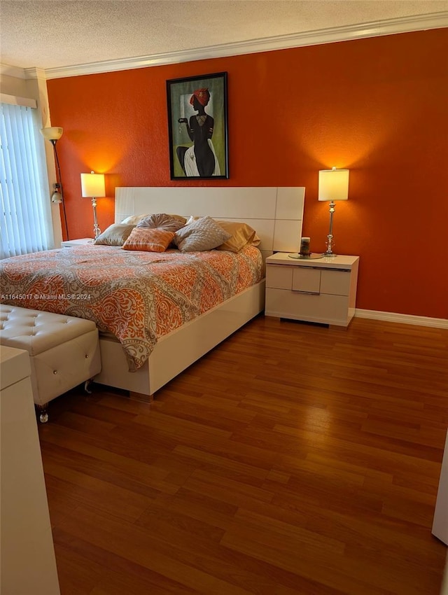 bedroom with baseboards, a textured ceiling, ornamental molding, and wood finished floors