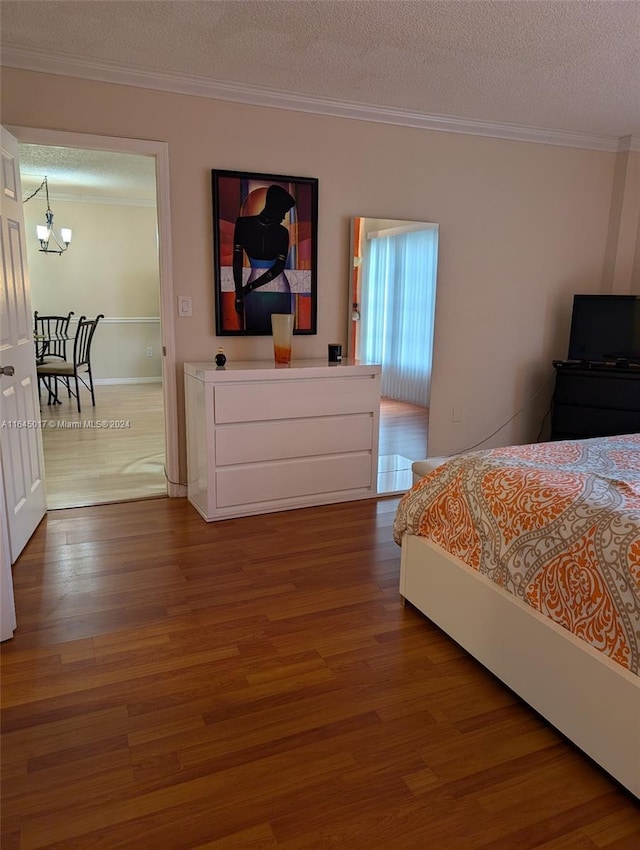 bedroom with ornamental molding, a chandelier, a textured ceiling, and wood finished floors