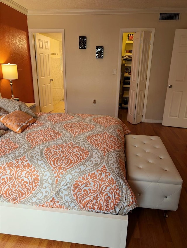 bedroom featuring ornamental molding, visible vents, connected bathroom, and wood finished floors