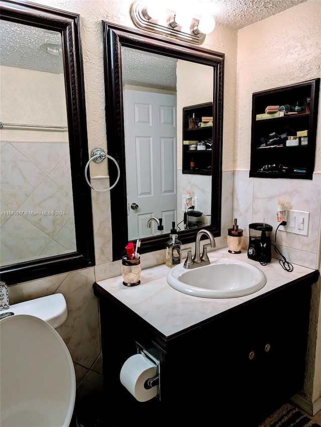 half bath featuring a textured wall, a textured ceiling, tile walls, and vanity