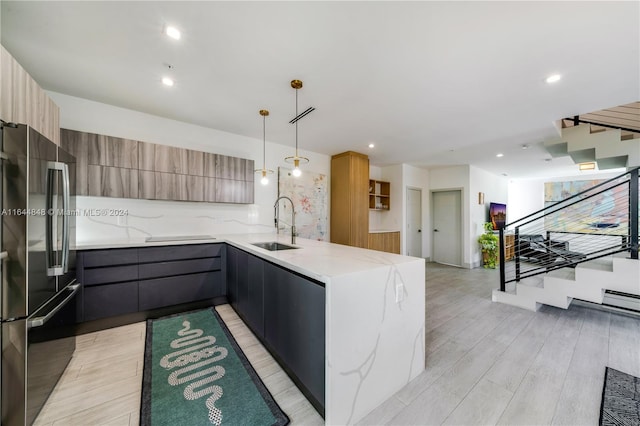 kitchen with light hardwood / wood-style flooring, hanging light fixtures, light stone counters, sink, and stainless steel fridge