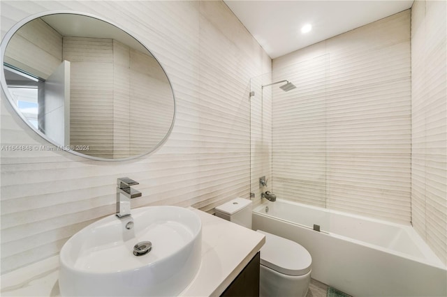 full bathroom featuring tiled shower / bath, toilet, vanity, and tile walls