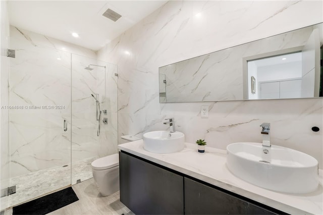 bathroom featuring tile patterned floors, an enclosed shower, double sink vanity, tile walls, and toilet