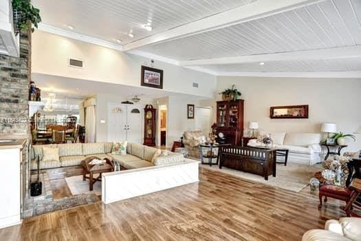 living room with light wood-type flooring, high vaulted ceiling, beamed ceiling, and brick wall