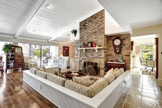 living room with wood-type flooring, a healthy amount of sunlight, a brick fireplace, and beam ceiling