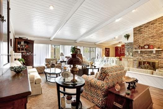 living room featuring a brick fireplace, light hardwood / wood-style flooring, and vaulted ceiling with beams