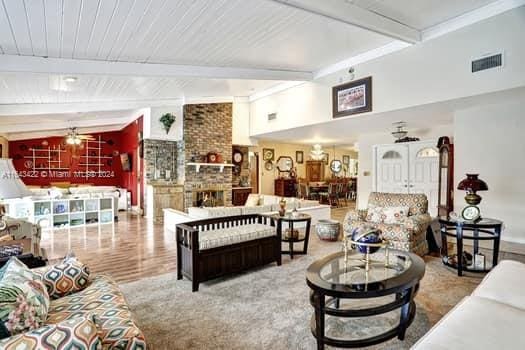 living room featuring hardwood / wood-style floors, a large fireplace, ceiling fan, lofted ceiling with beams, and brick wall