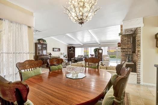 dining area featuring a notable chandelier, light tile patterned floors, a wood stove, vaulted ceiling with beams, and brick wall