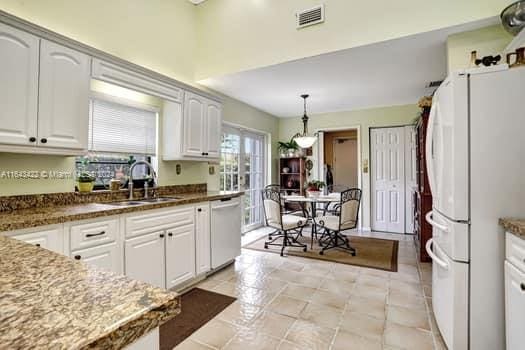 kitchen featuring white refrigerator, white cabinetry, stainless steel dishwasher, and light tile patterned flooring