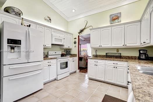 kitchen featuring vaulted ceiling, light tile patterned floors, white appliances, and white cabinets