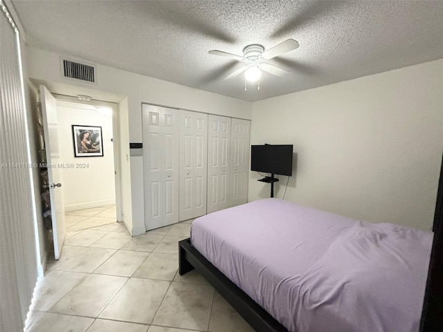 bedroom with ceiling fan, light tile patterned floors, a closet, and a textured ceiling