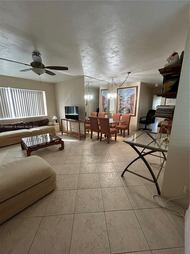 tiled living room with ceiling fan with notable chandelier and a textured ceiling