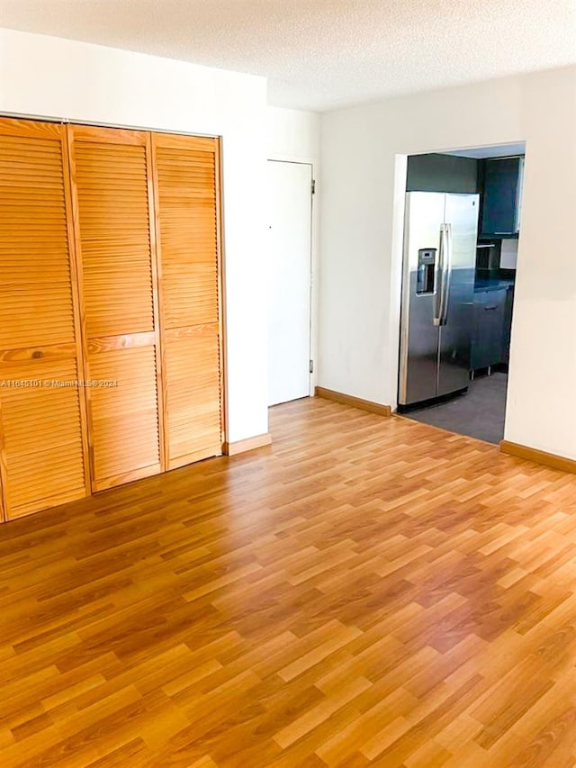 unfurnished bedroom with light wood-type flooring, stainless steel refrigerator with ice dispenser, a closet, and a textured ceiling