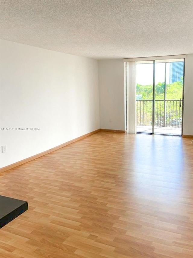 spare room featuring a wall of windows, light hardwood / wood-style flooring, and a textured ceiling