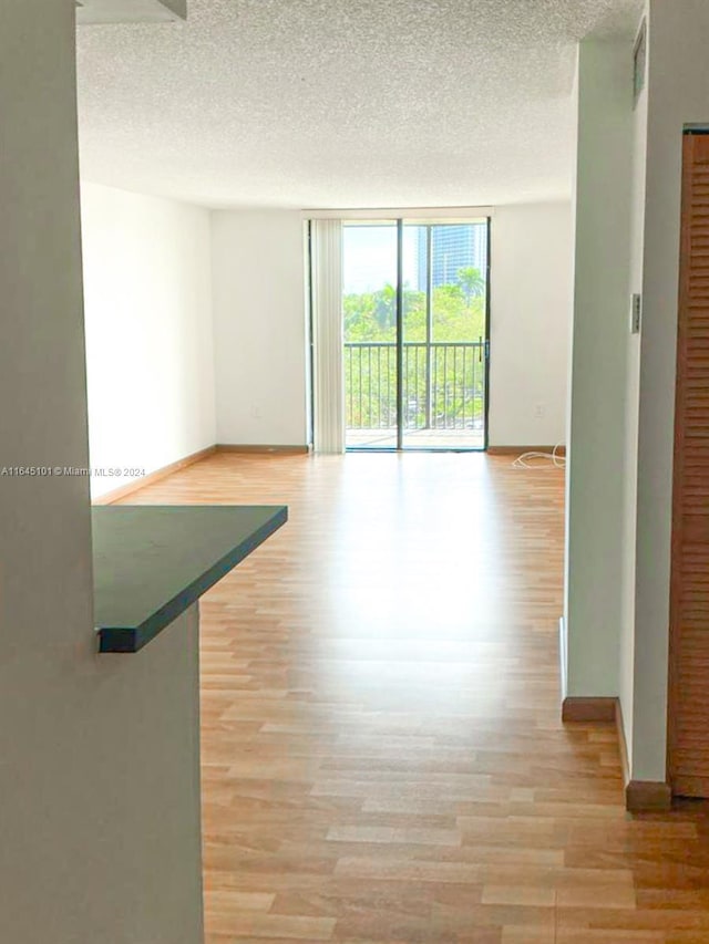 empty room with light wood-style flooring, baseboards, a wall of windows, and a textured ceiling