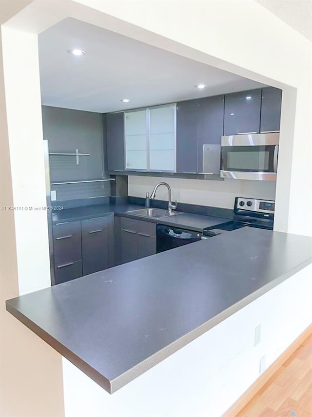 kitchen with a peninsula, a sink, appliances with stainless steel finishes, dark countertops, and modern cabinets