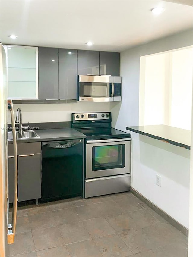 kitchen with appliances with stainless steel finishes, gray cabinets, dark countertops, and a sink