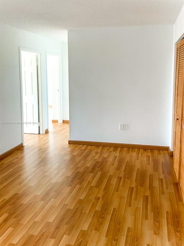 empty room featuring a textured ceiling, baseboards, and light wood-style floors