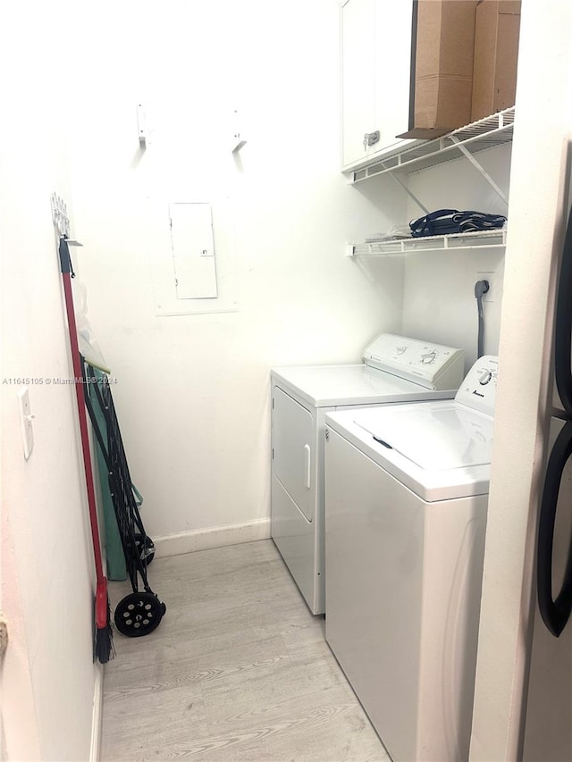 clothes washing area with light wood-type flooring, washing machine and clothes dryer, and cabinets