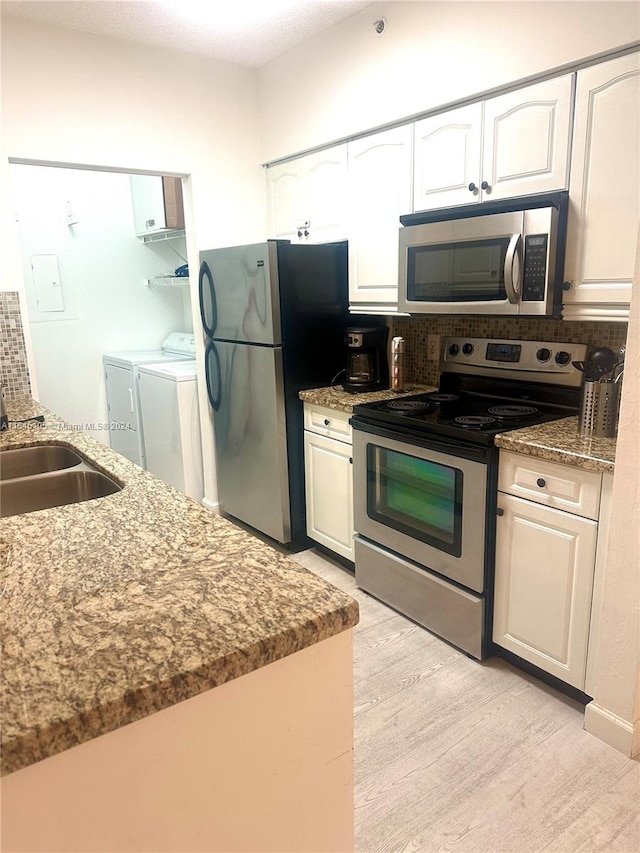 kitchen with white cabinets, light wood-type flooring, stainless steel appliances, sink, and washer and clothes dryer