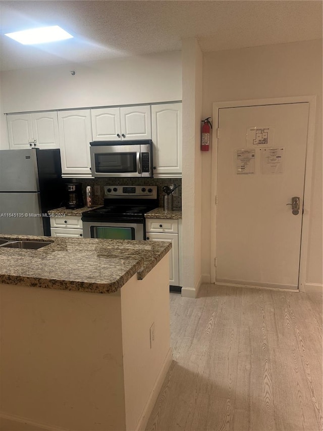 kitchen with appliances with stainless steel finishes, light hardwood / wood-style floors, white cabinetry, dark stone counters, and a textured ceiling