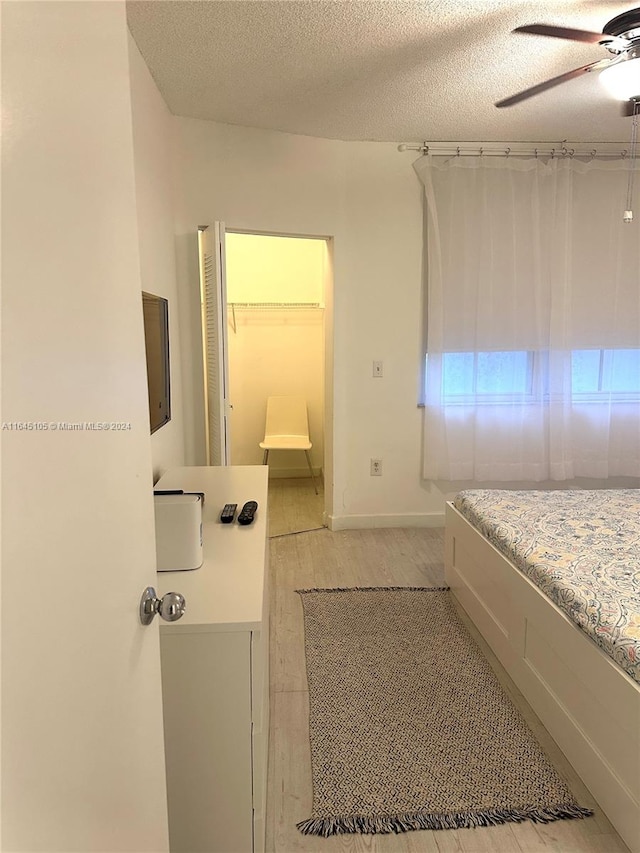 bedroom featuring a textured ceiling, a spacious closet, ceiling fan, and light hardwood / wood-style floors