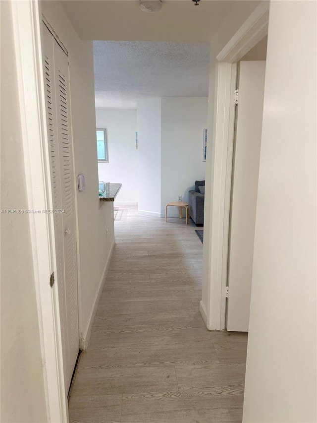 corridor with a textured ceiling and light wood-type flooring