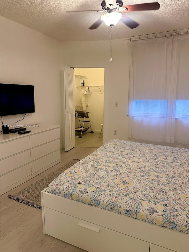 bedroom featuring a textured ceiling, a spacious closet, a closet, ceiling fan, and light wood-type flooring