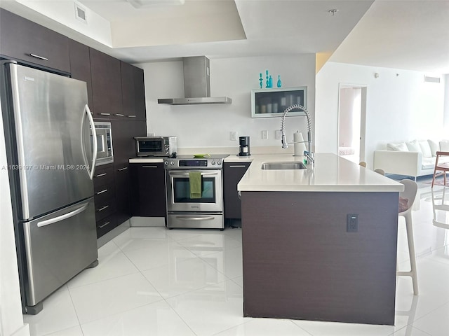 kitchen with wall chimney exhaust hood, sink, stainless steel appliances, light tile patterned flooring, and dark brown cabinets