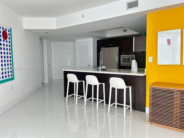 kitchen with appliances with stainless steel finishes, light tile patterned floors, and a kitchen bar