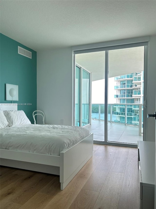 bedroom featuring light hardwood / wood-style floors, access to outside, expansive windows, and a textured ceiling