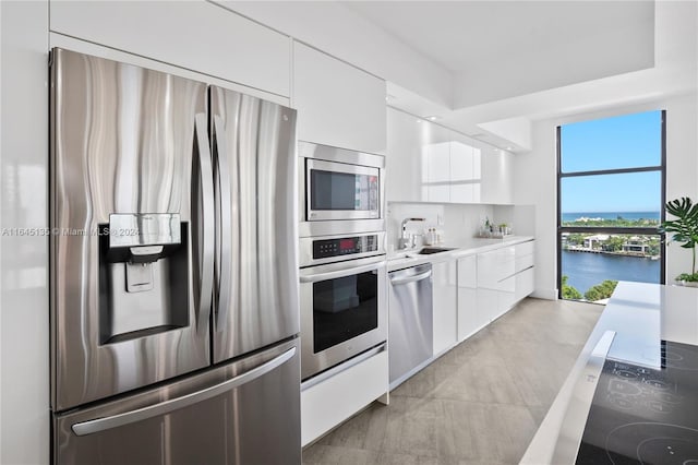 kitchen with appliances with stainless steel finishes, white cabinetry, sink, a water view, and light tile patterned floors