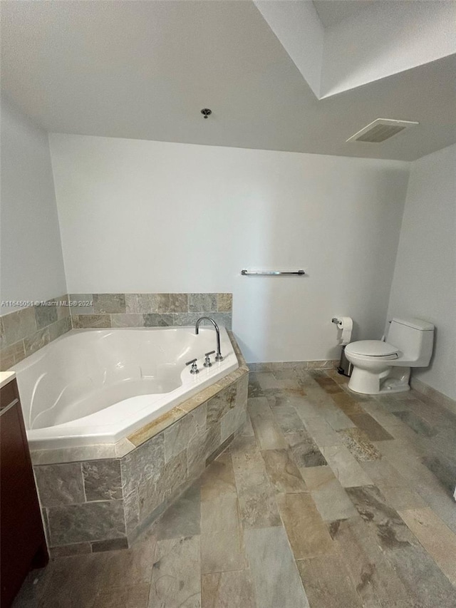 bathroom featuring tile patterned flooring, toilet, tiled bath, and vanity