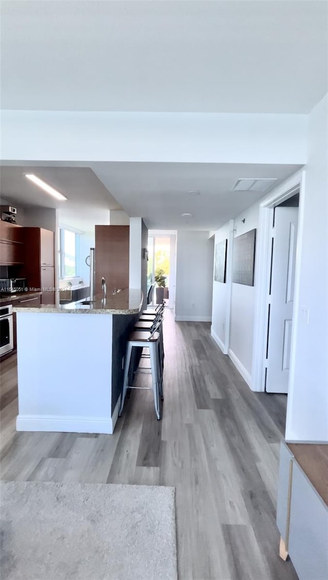 kitchen featuring a breakfast bar, light stone countertops, oven, and wood-type flooring