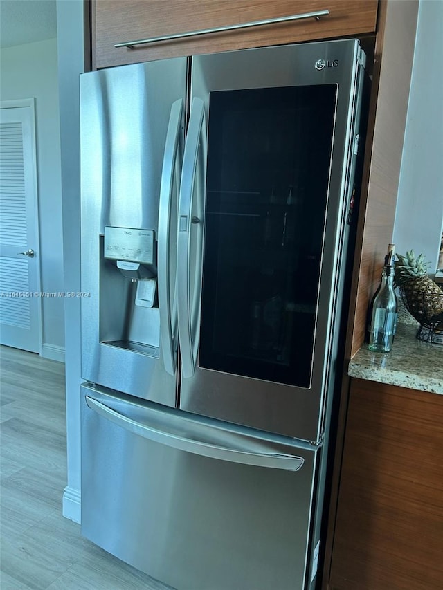 details with stainless steel fridge with ice dispenser, light wood-type flooring, and light stone counters