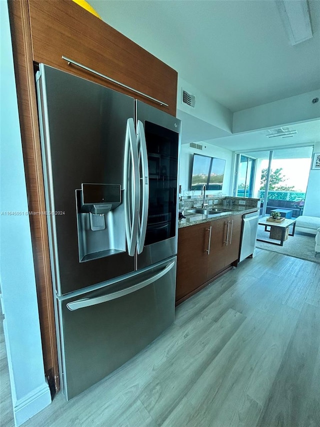 kitchen with appliances with stainless steel finishes, light hardwood / wood-style flooring, stone countertops, and sink