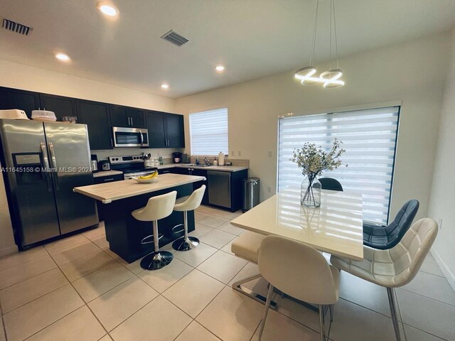 kitchen with appliances with stainless steel finishes, pendant lighting, a kitchen island, a breakfast bar area, and light tile patterned flooring