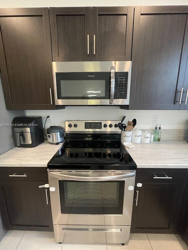 kitchen featuring appliances with stainless steel finishes, light stone countertops, dark brown cabinets, and light tile patterned floors