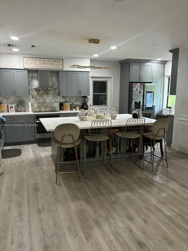 kitchen featuring backsplash, gray cabinetry, light hardwood / wood-style floors, and wall chimney range hood