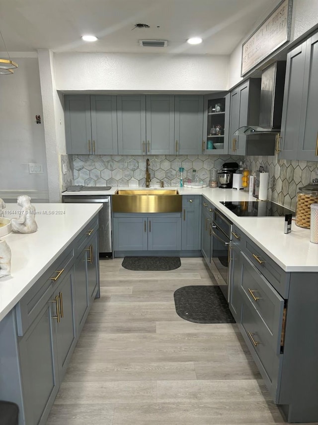 kitchen with black electric stovetop, oven, wall chimney range hood, sink, and tasteful backsplash