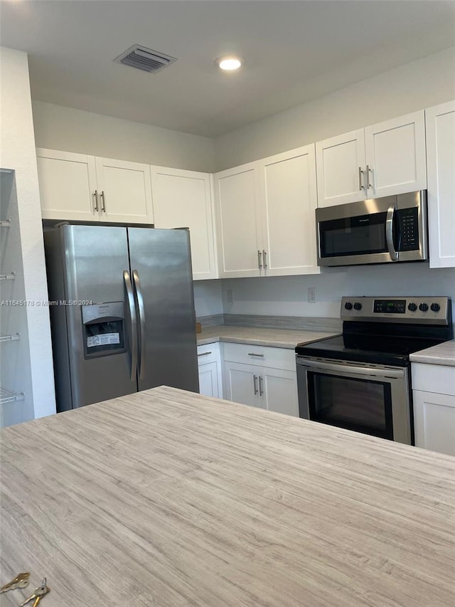 kitchen with stainless steel appliances, hardwood / wood-style floors, and white cabinetry