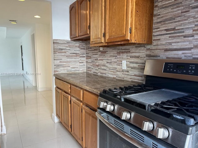 kitchen featuring light tile patterned floors, stone countertops, decorative backsplash, and stainless steel gas range